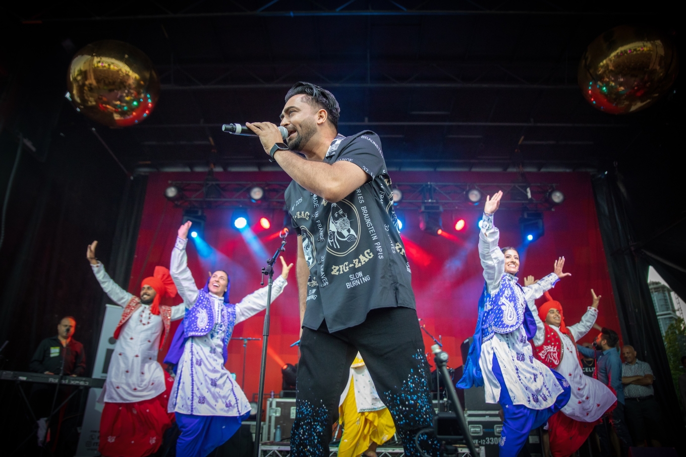 Sharry Mann sings on stage with bhangra dancers behind him. 